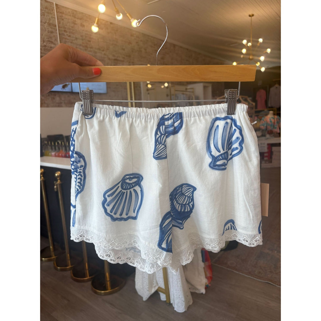 White shorts with blue shell patterns on a hanger indoors.