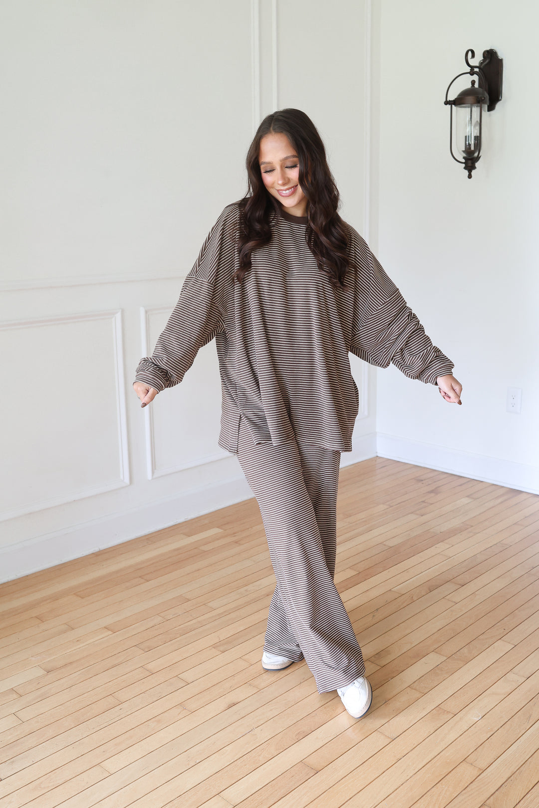 A woman modeling a matching two-piece lounge set consisting of a textured, long-sleeve cropped sweatshirt and wide-leg pants in a brown color.