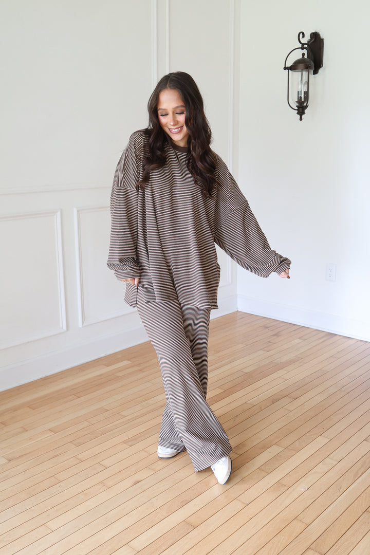 A woman modeling a matching two-piece lounge set consisting of a textured, ribbed long-sleeve top and wide-leg pants in a brown color