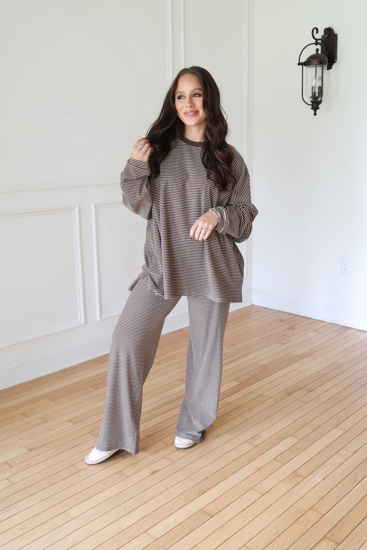 A woman modeling a matching two-piece lounge set consisting of a long-sleeve ribbed top and wide-leg pants in a brown color