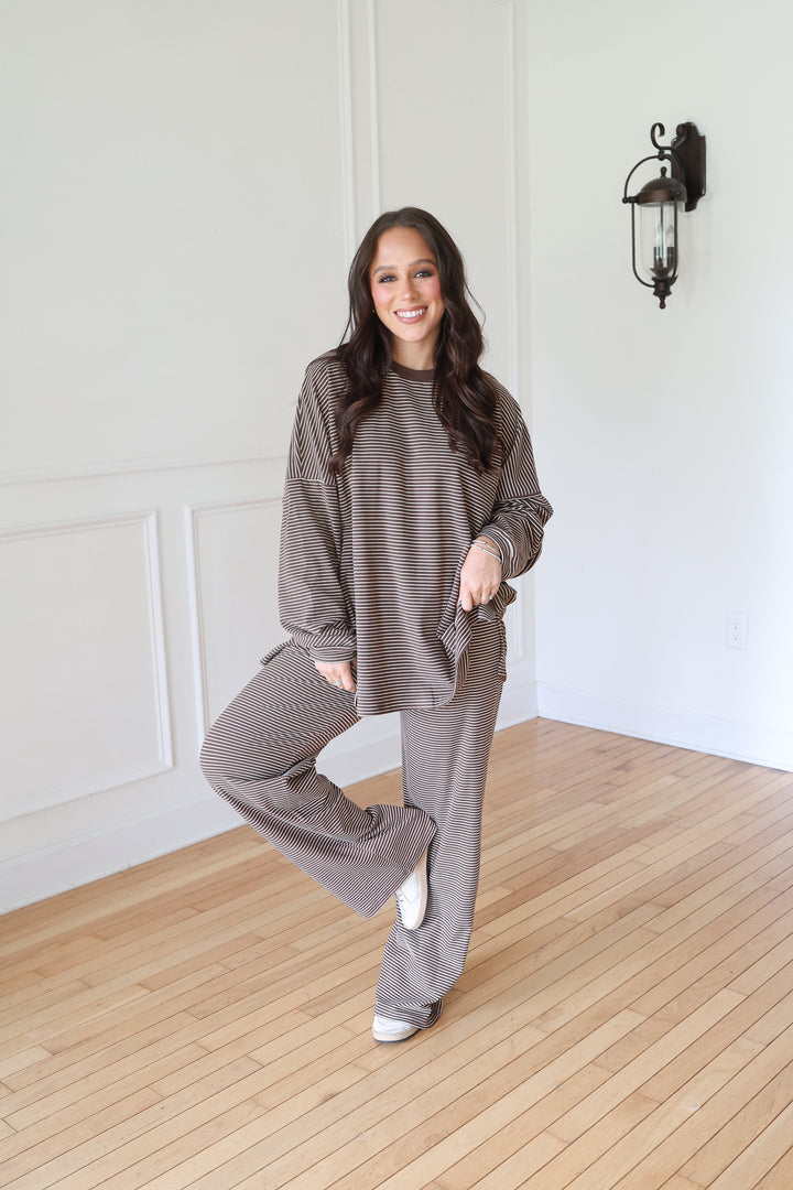 A woman modeling a matching two-piece lounge set consisting of a textured long-sleeve top and wide-leg pants in a brown color