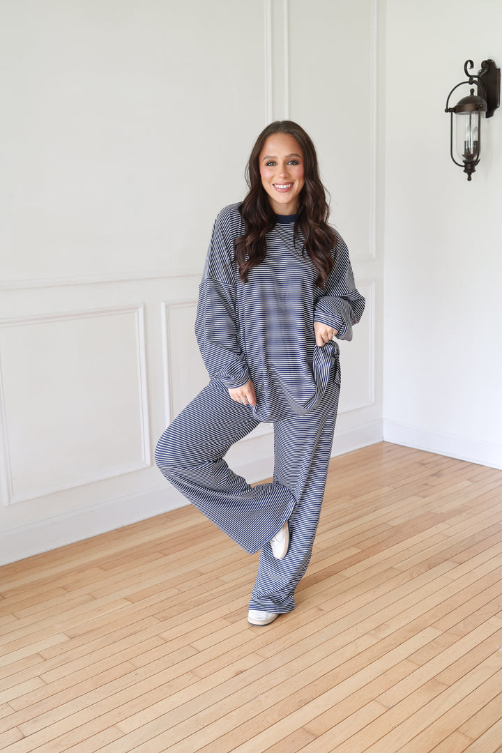 A woman modeling a matching navy lounge set consisting of a long-sleeve top and wide-leg pants