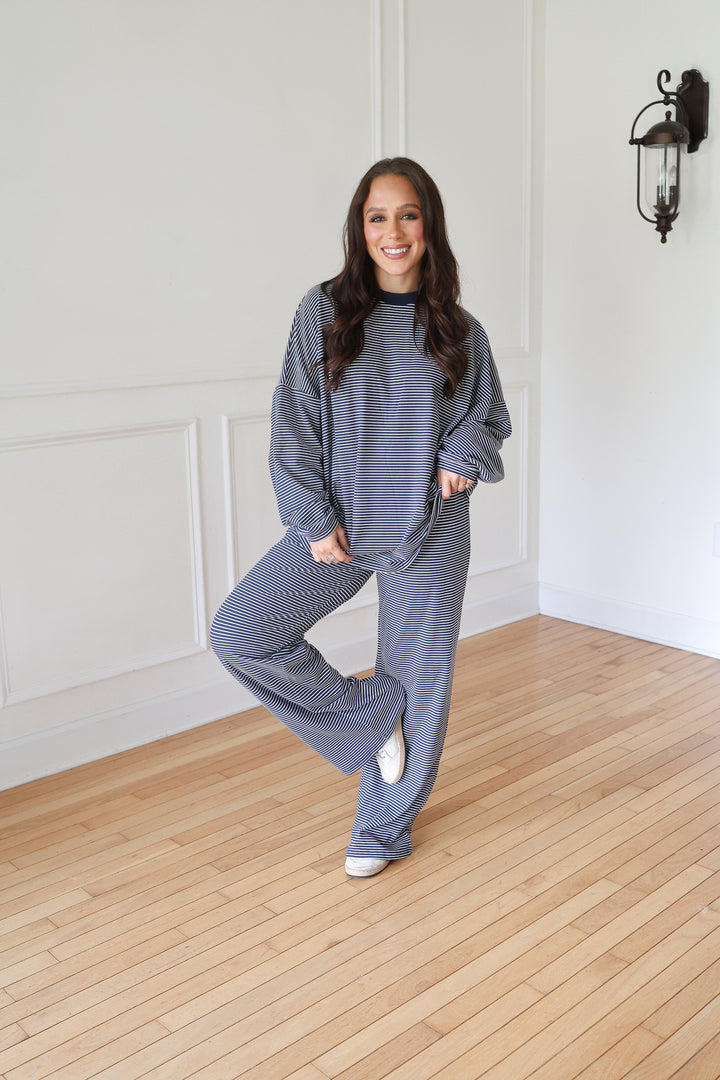 A woman modeling a matching navy lounge set consisting of a long-sleeve top and wide-leg pants