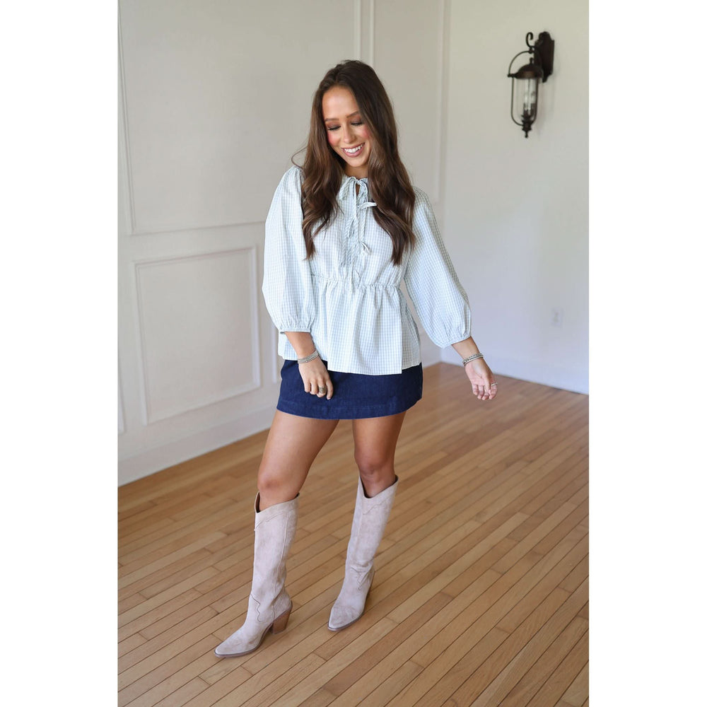Woman wearing a white blouse, blue skirt, and white knee-high boots 