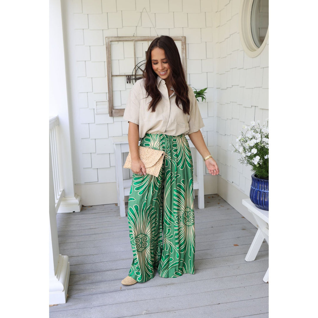 Woman wearing a beige blouse and green patterned pants on a wooden deck.