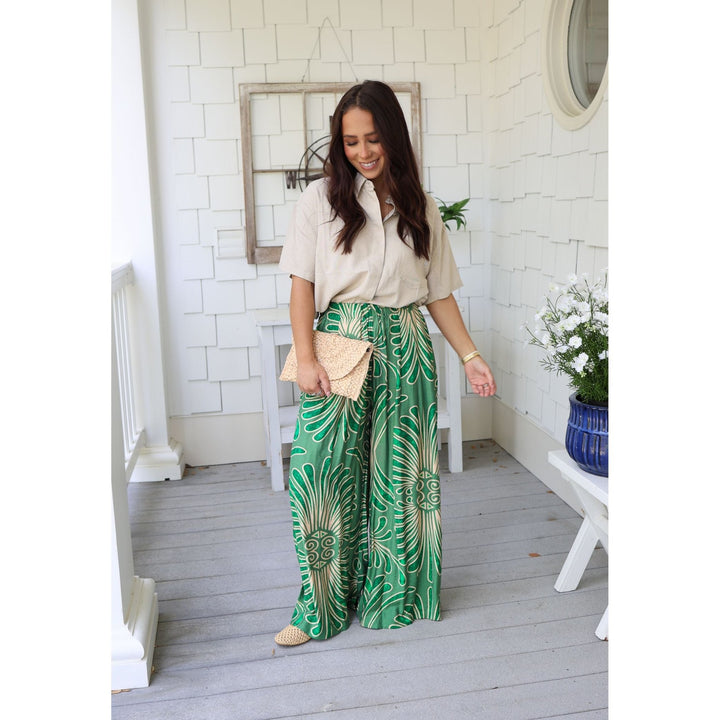 Woman wearing a beige blouse and green patterned pants on a wooden deck.