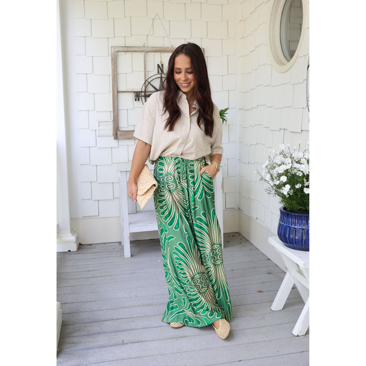 Woman wearing a beige shirt and green patterned pants on a wooden deck.