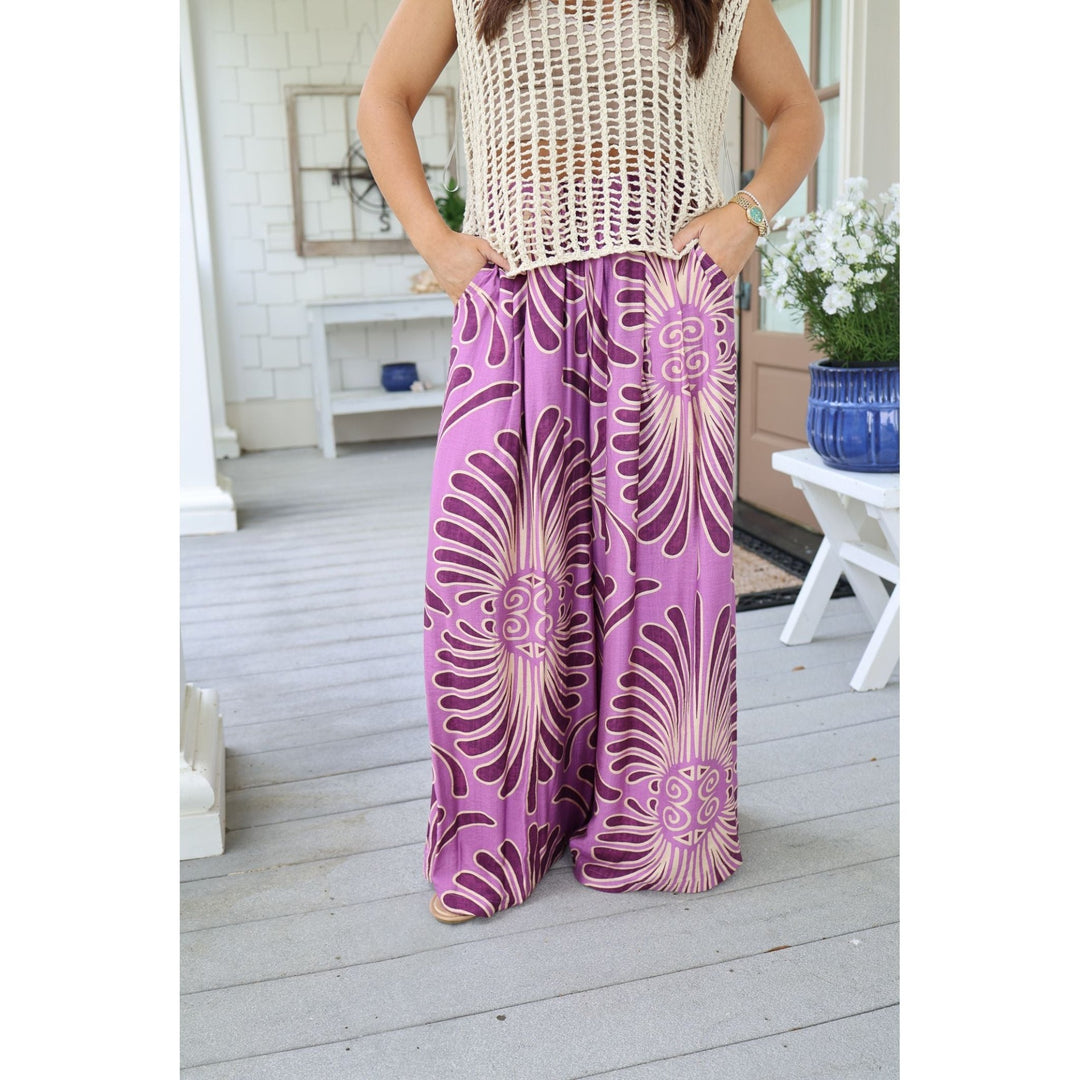 Person wearing a sleeveless top and purple patterned pants on a wooden deck.