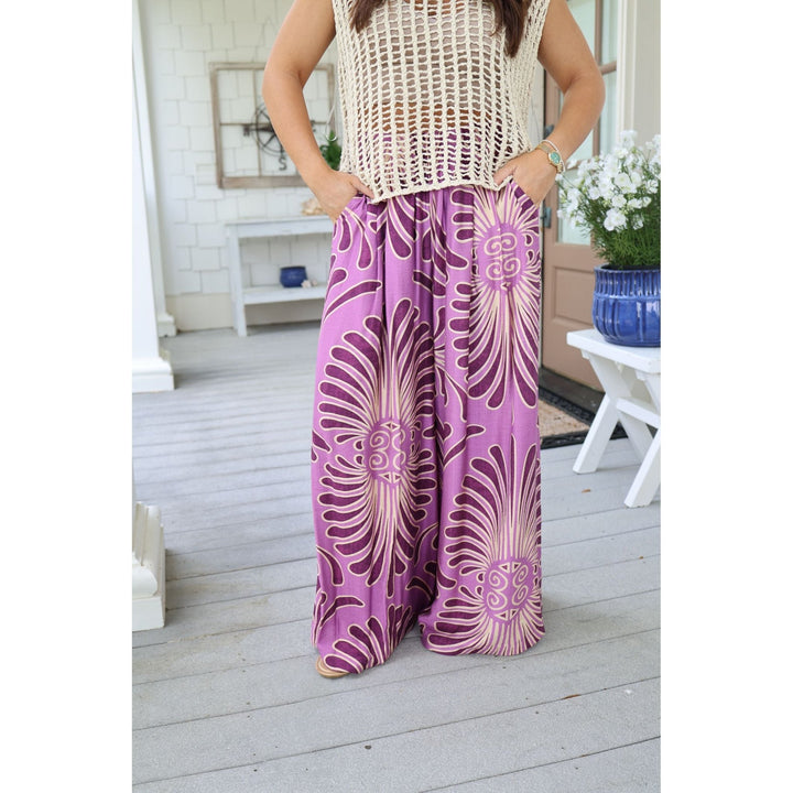 Person wearing a sleeveless top and purple patterned pants on a wooden deck.