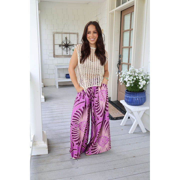 Woman in a patterned outfit standing on a porch with a white wall and wooden door in the background.