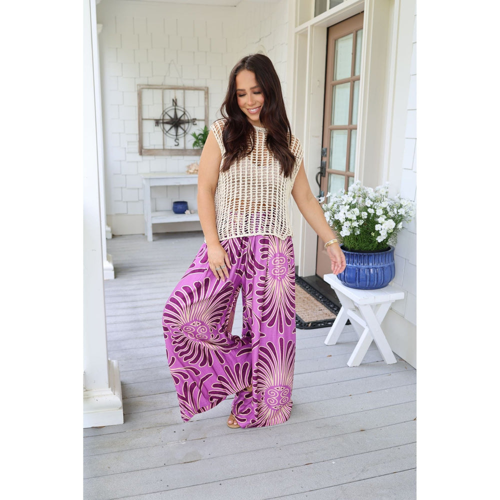 Woman wearing a beige top and purple patterned pants on a porch.