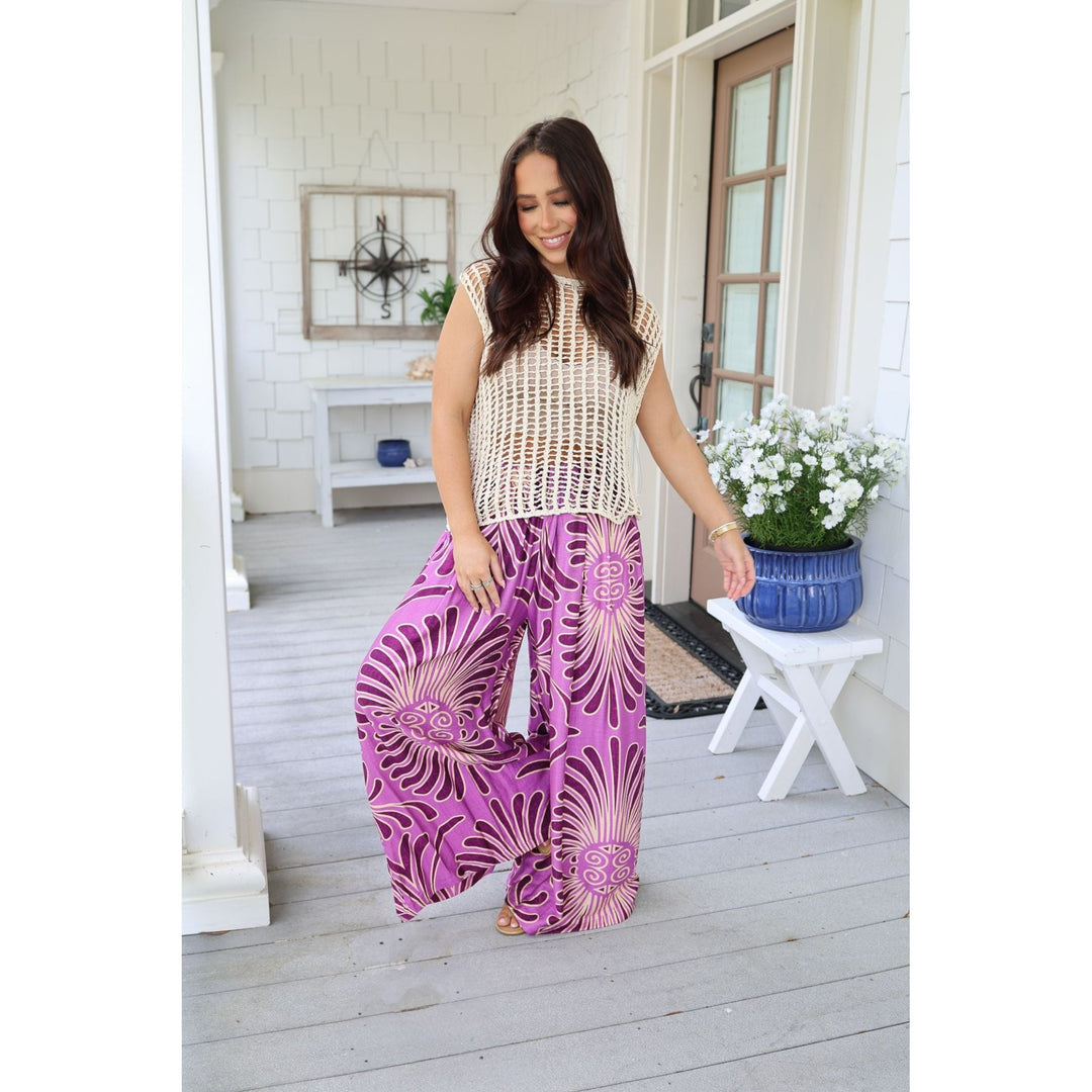 Woman wearing a beige top and purple patterned pants on a porch.