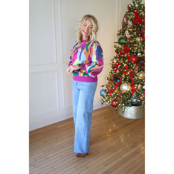 Woman wearing a colorful sweater and blue jeans standing next to a Christmas tree.