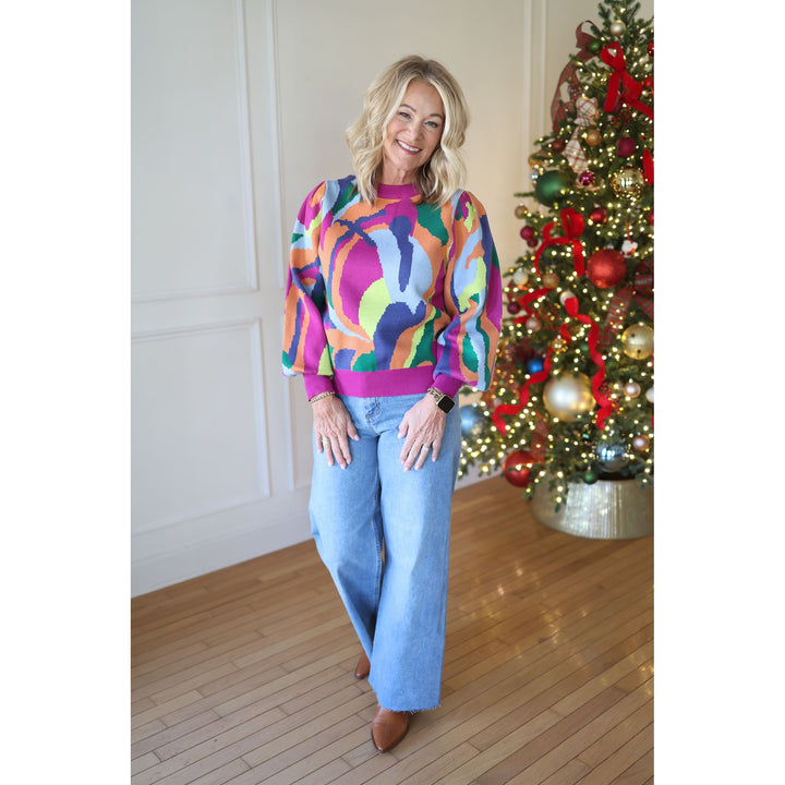 Woman wearing a colorful sweater and jeans standing in front of a decorated Christmas tree.