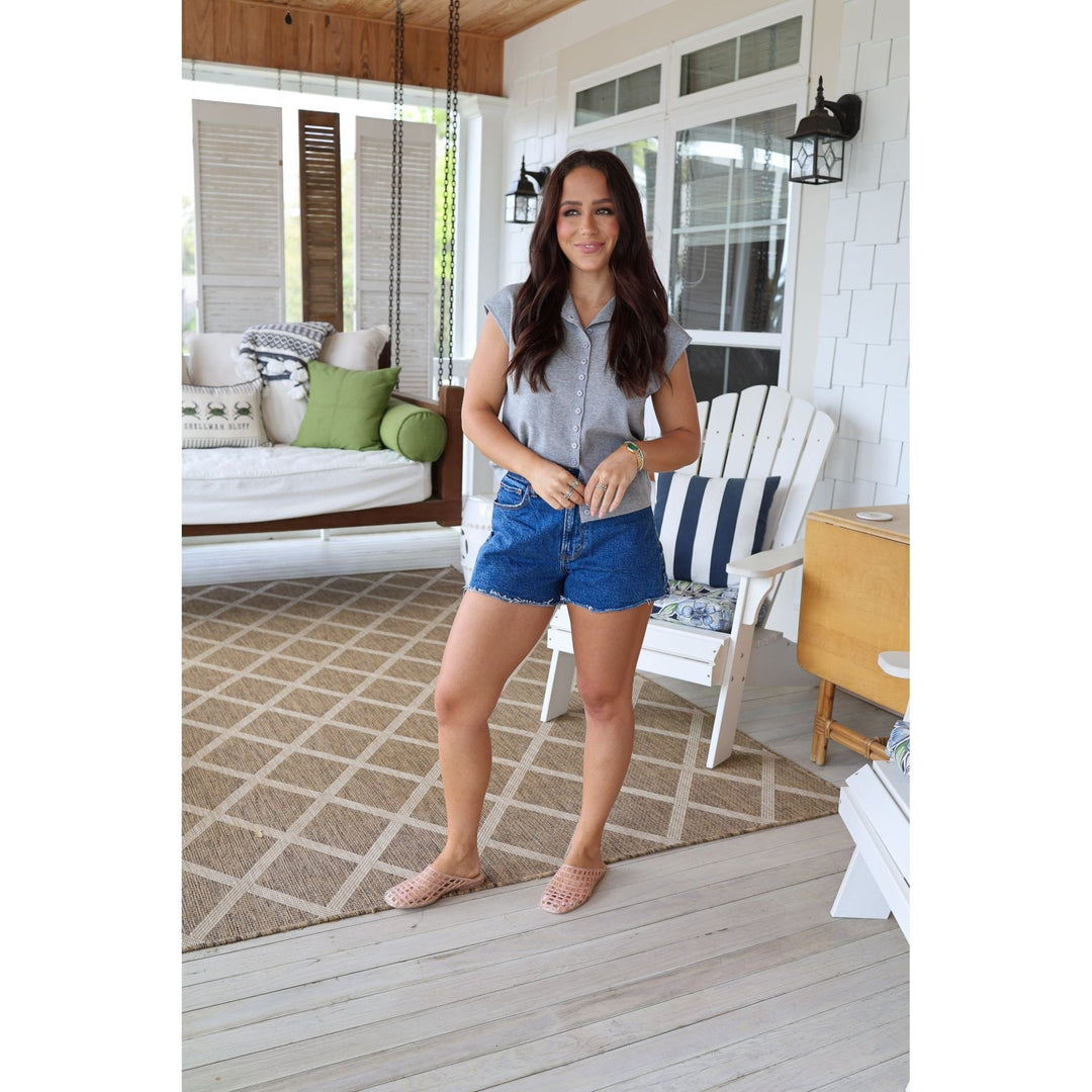 Woman standing on a porch wearing a gray shirt and blue shorts