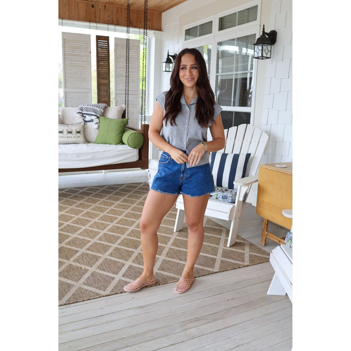 Woman standing on a porch wearing a gray shirt and blue shorts