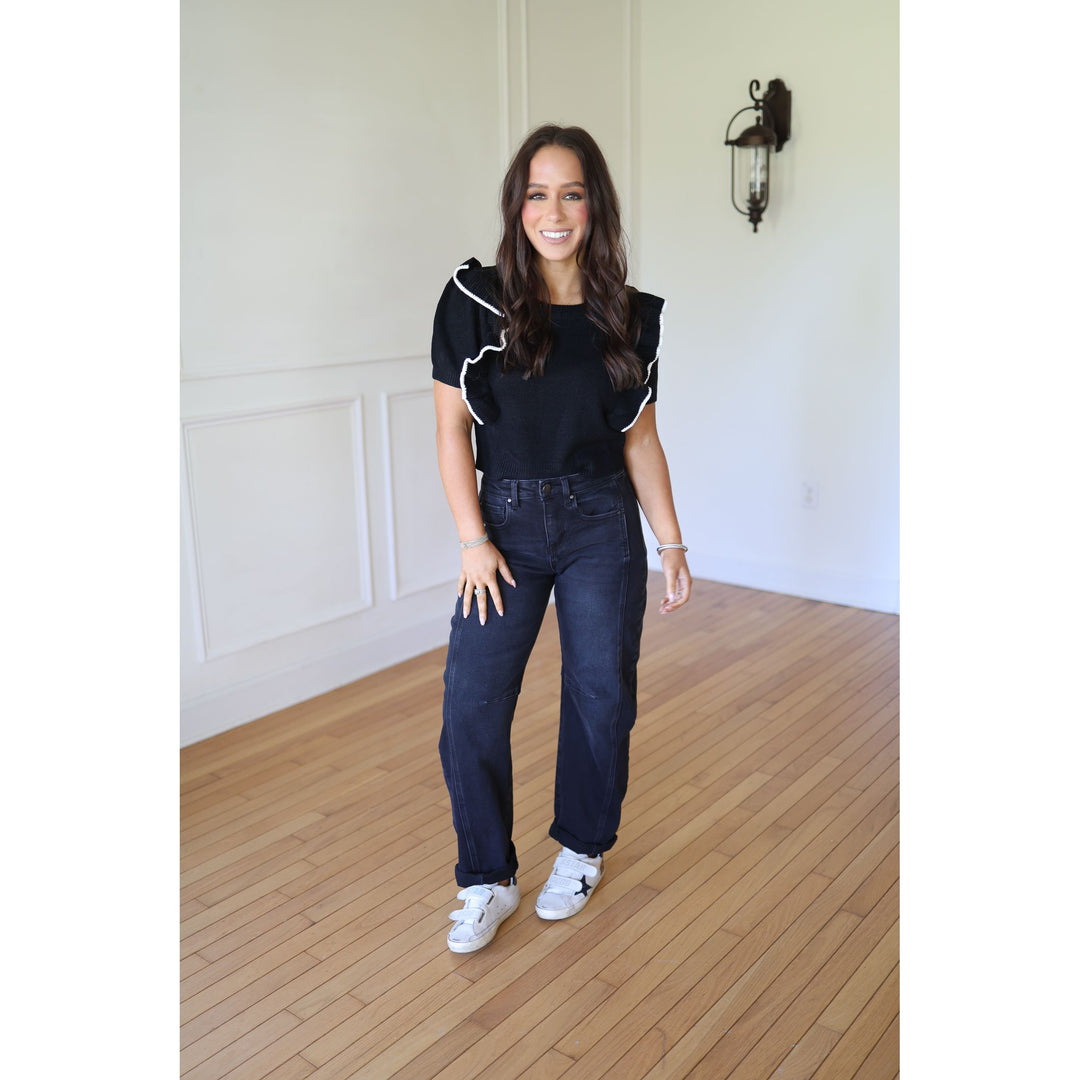 Woman wearing a black top with white trim and dark jeans 