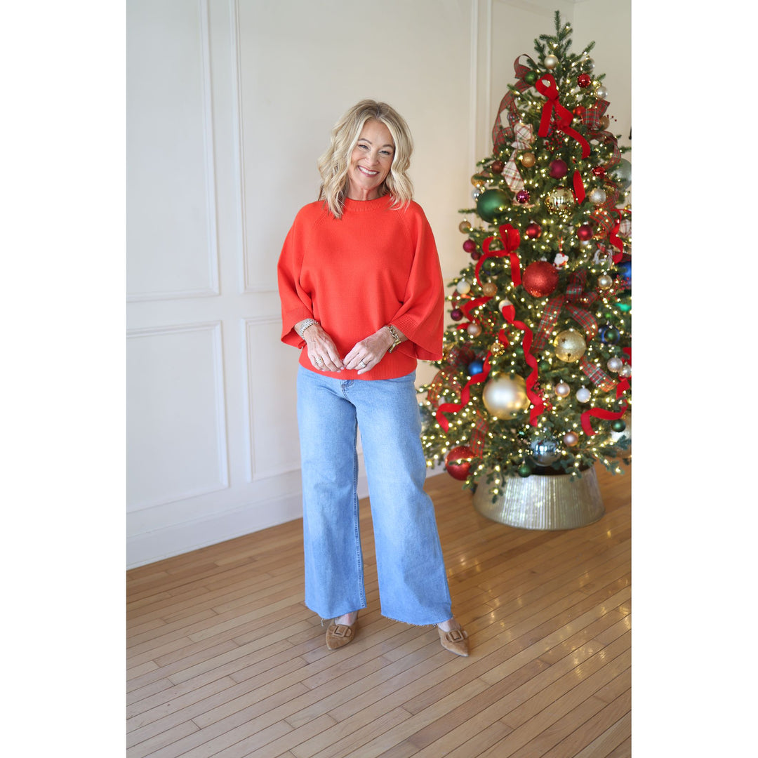 Woman in a red sweater and blue jeans standing in front of a decorated Christmas tree.
