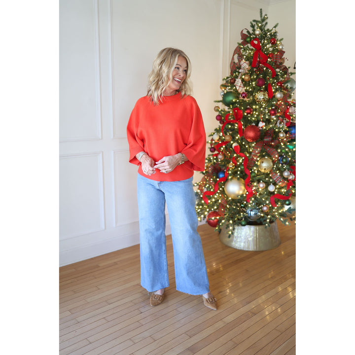 Person wearing a red sweater and blue jeans standing in front of a decorated Christmas tree.