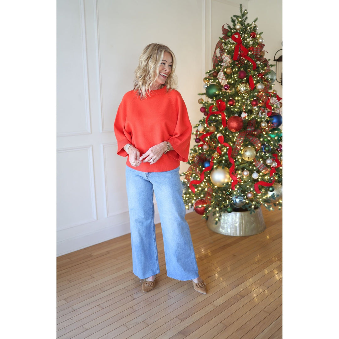Woman in a red sweater and blue jeans standing next to a decorated Christmas tree.