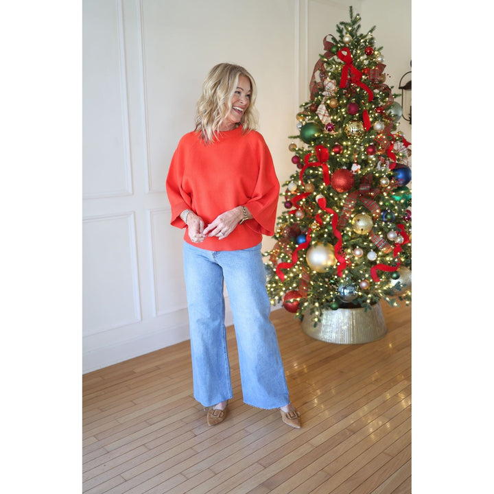 Woman in a red sweater and blue jeans standing next to a decorated Christmas tree.