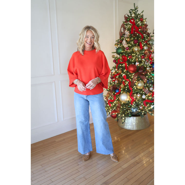 Woman in a red sweater and blue jeans standing next to a decorated Christmas tree.