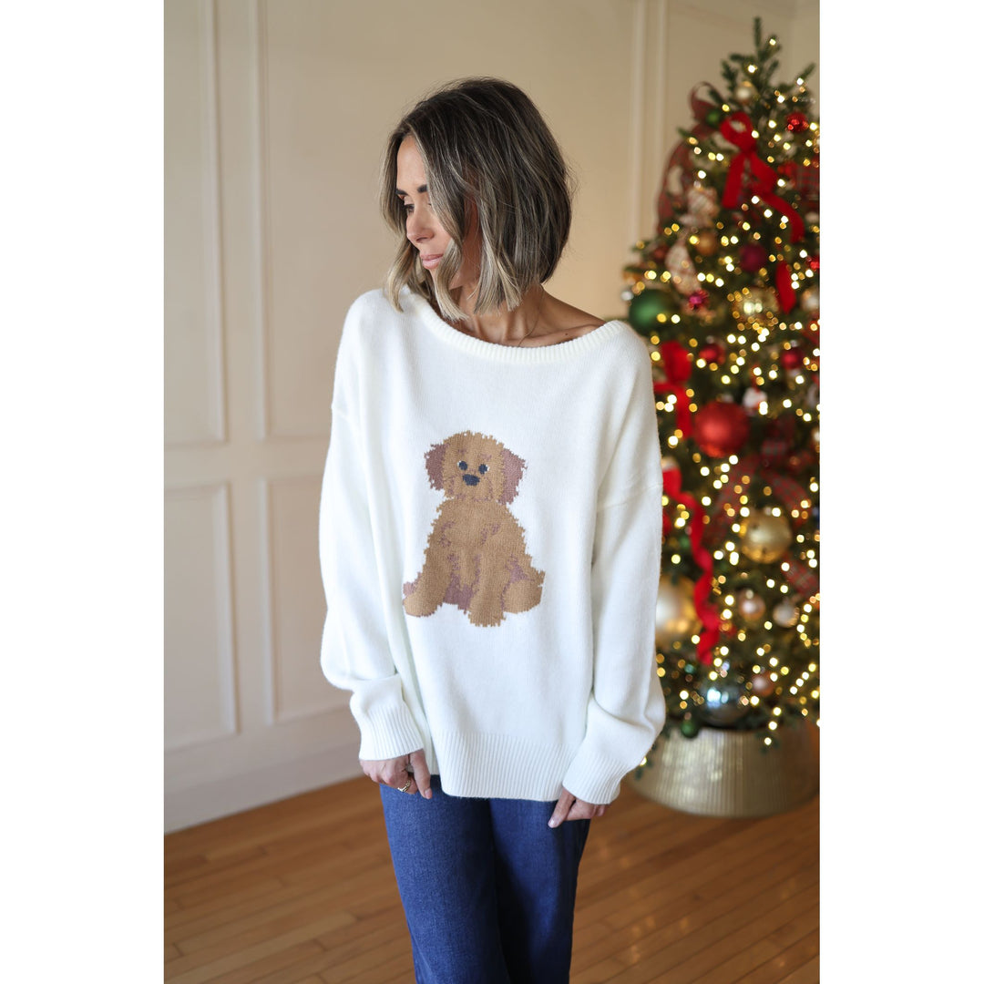 Woman wearing a white sweater with a dog design in front of a decorated Christmas tree.