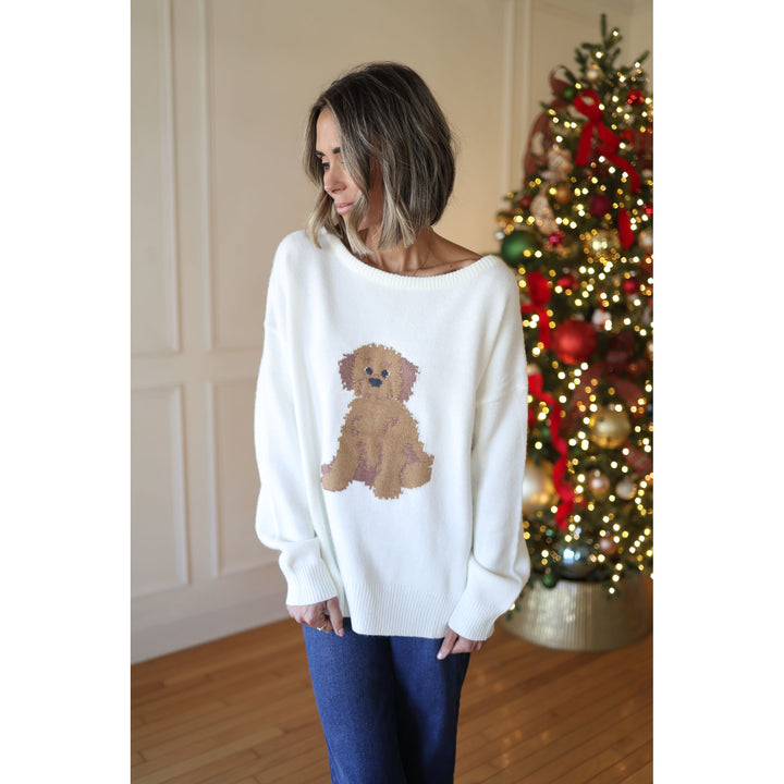 Woman wearing a white sweater with a dog design in front of a decorated Christmas tree.