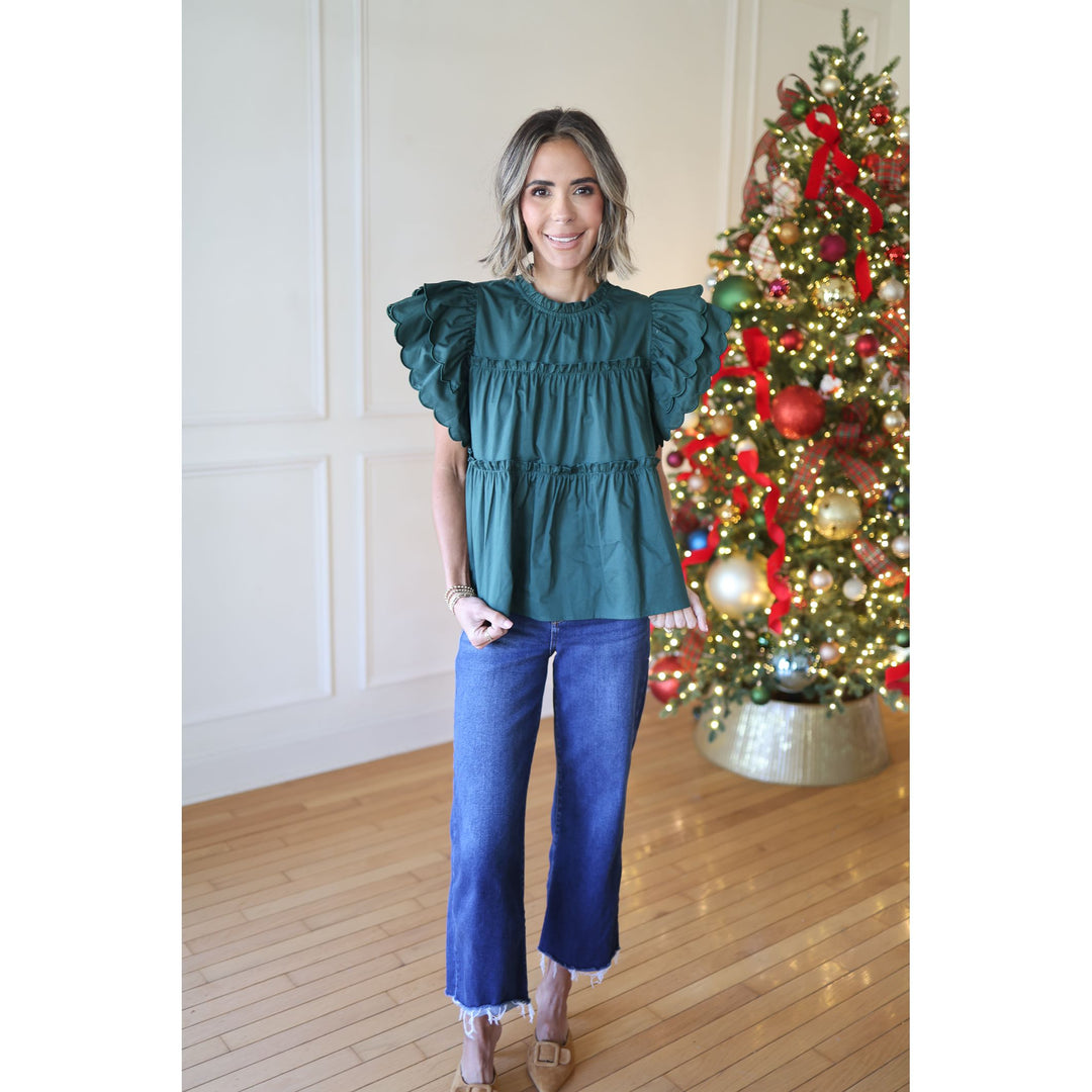 Woman wearing a teal top and blue jeans standing in front of a decorated Christmas tree.