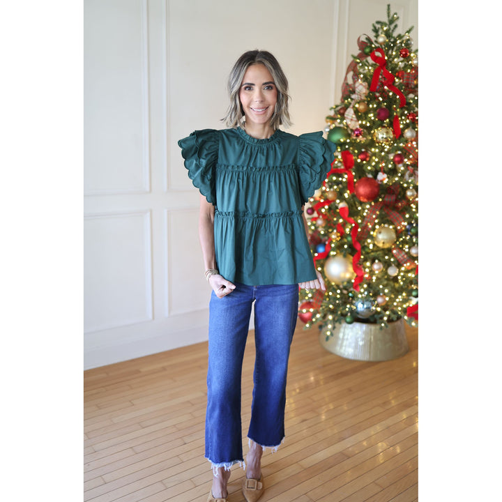 Woman wearing a teal top and blue jeans standing in front of a decorated Christmas tree.