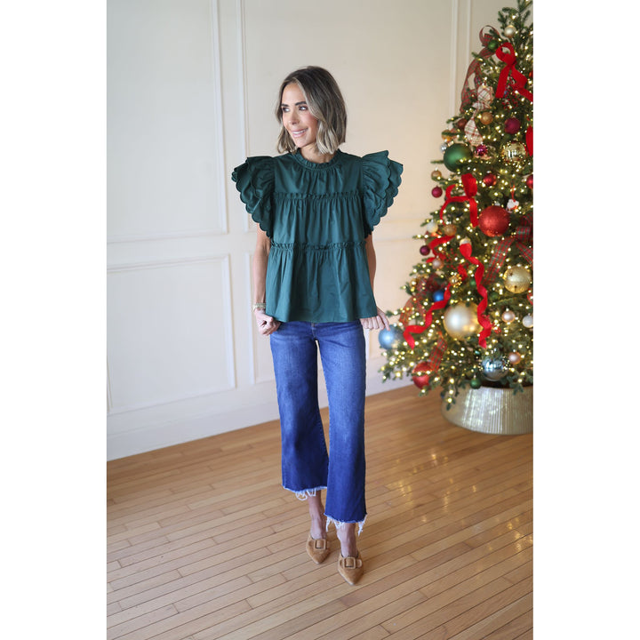 Woman wearing a green top and blue jeans standing in front of a decorated Christmas tree.