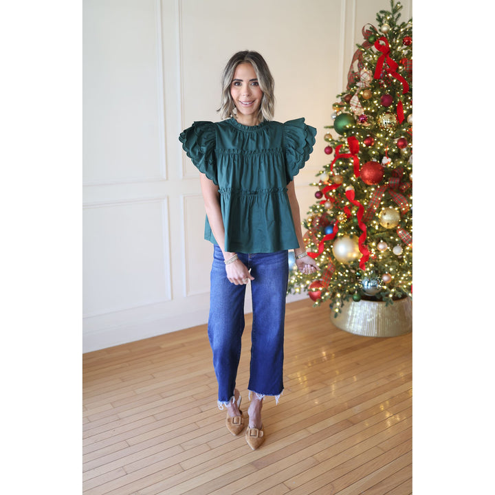 Woman wearing a green blouse and blue jeans standing in front of a decorated Christmas tree.