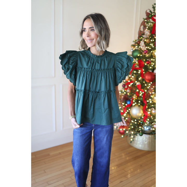Woman wearing a teal top and blue pants standing in front of a decorated Christmas tree.