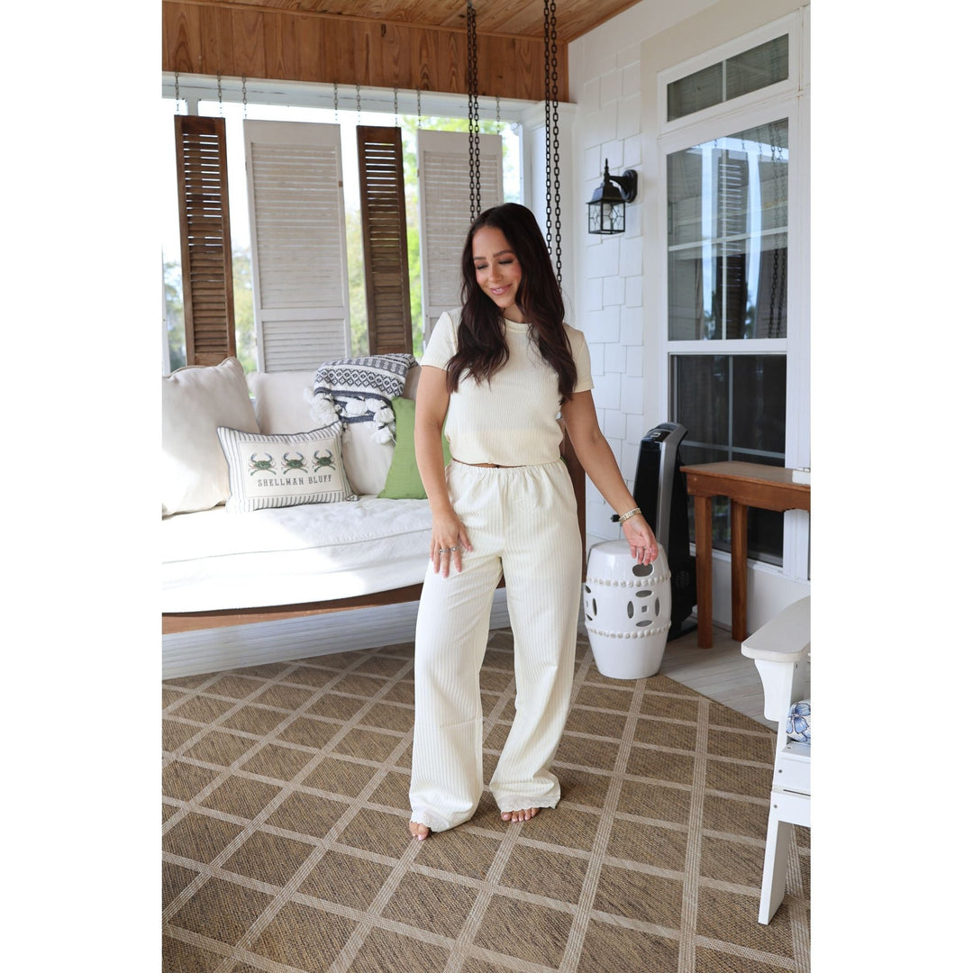 Woman in a white outfit standing in a living room with a couch and decorative pillows.