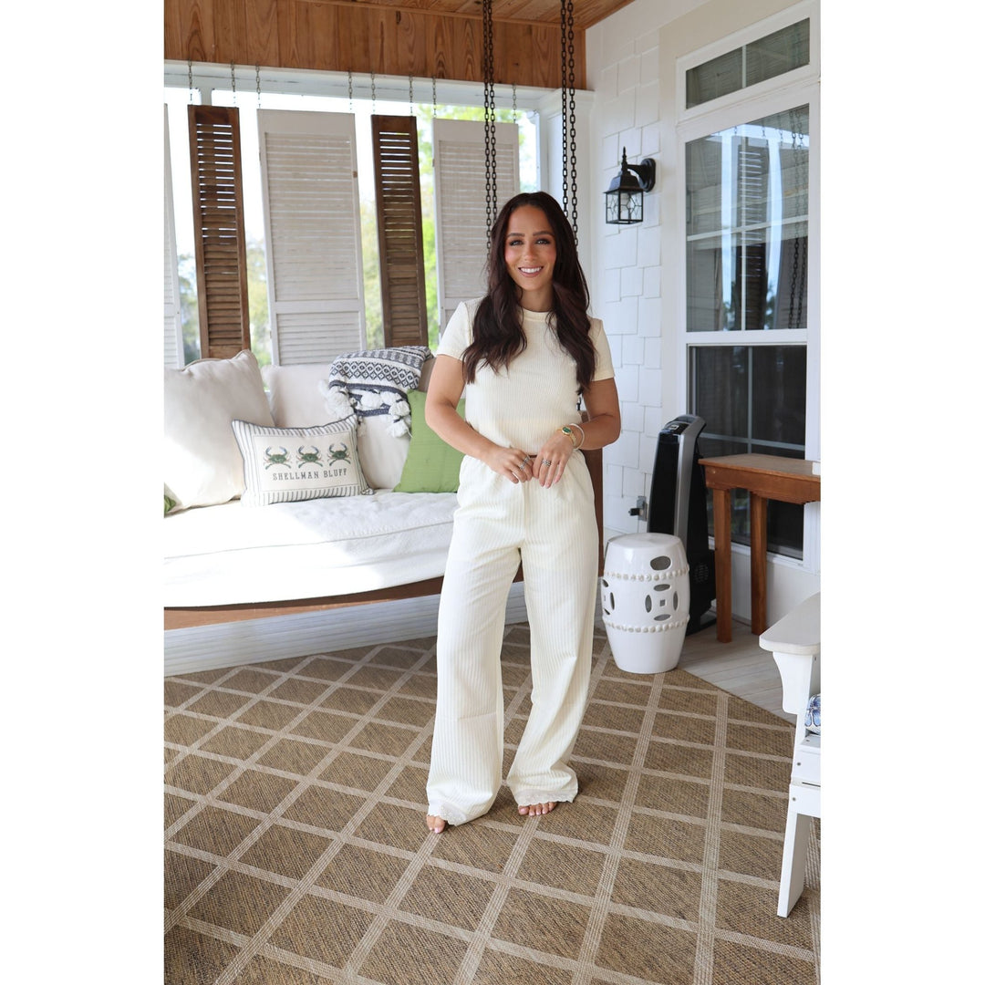 Woman in a white outfit standing on a patterned floor in a home setting.