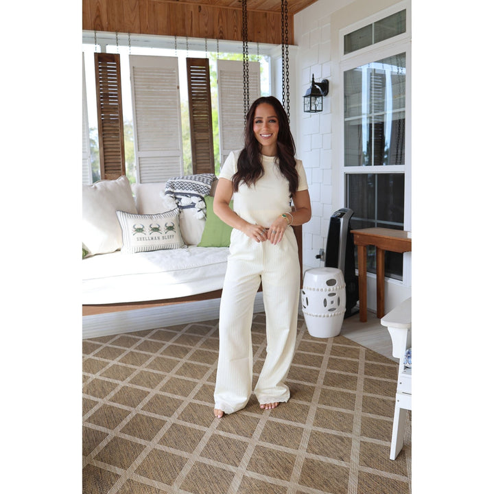 Woman in a white outfit standing on a patterned floor in a home setting.