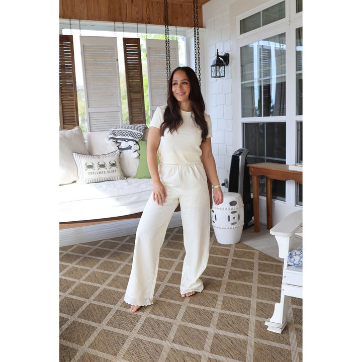 Woman in a white outfit standing on a patterned rug in a home setting.