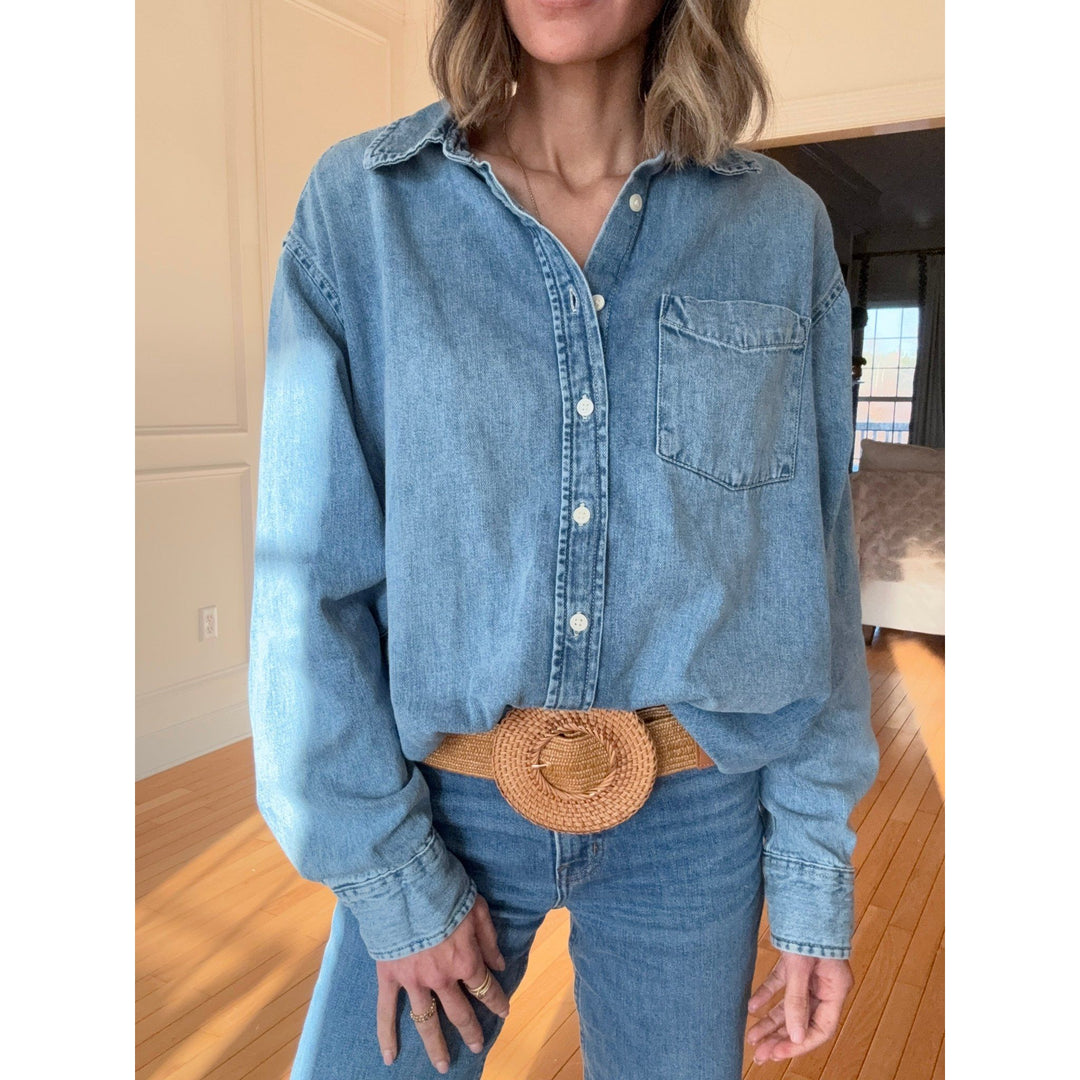 Person wearing a blue denim shirt and jeans with a woven belt indoors.