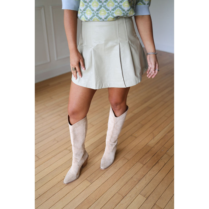 Person wearing a beige skirt and white knee-high boots 