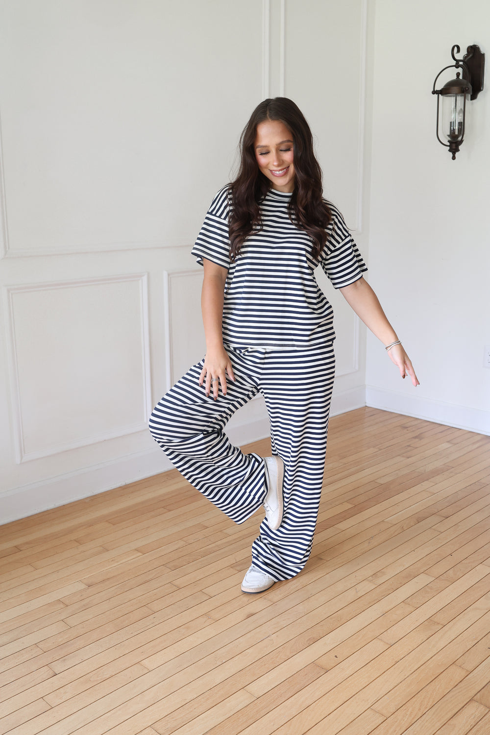 A woman modeling a matching navy and white horizontally striped lounge set, consisting of a short-sleeve t-shirt and wide-leg pants