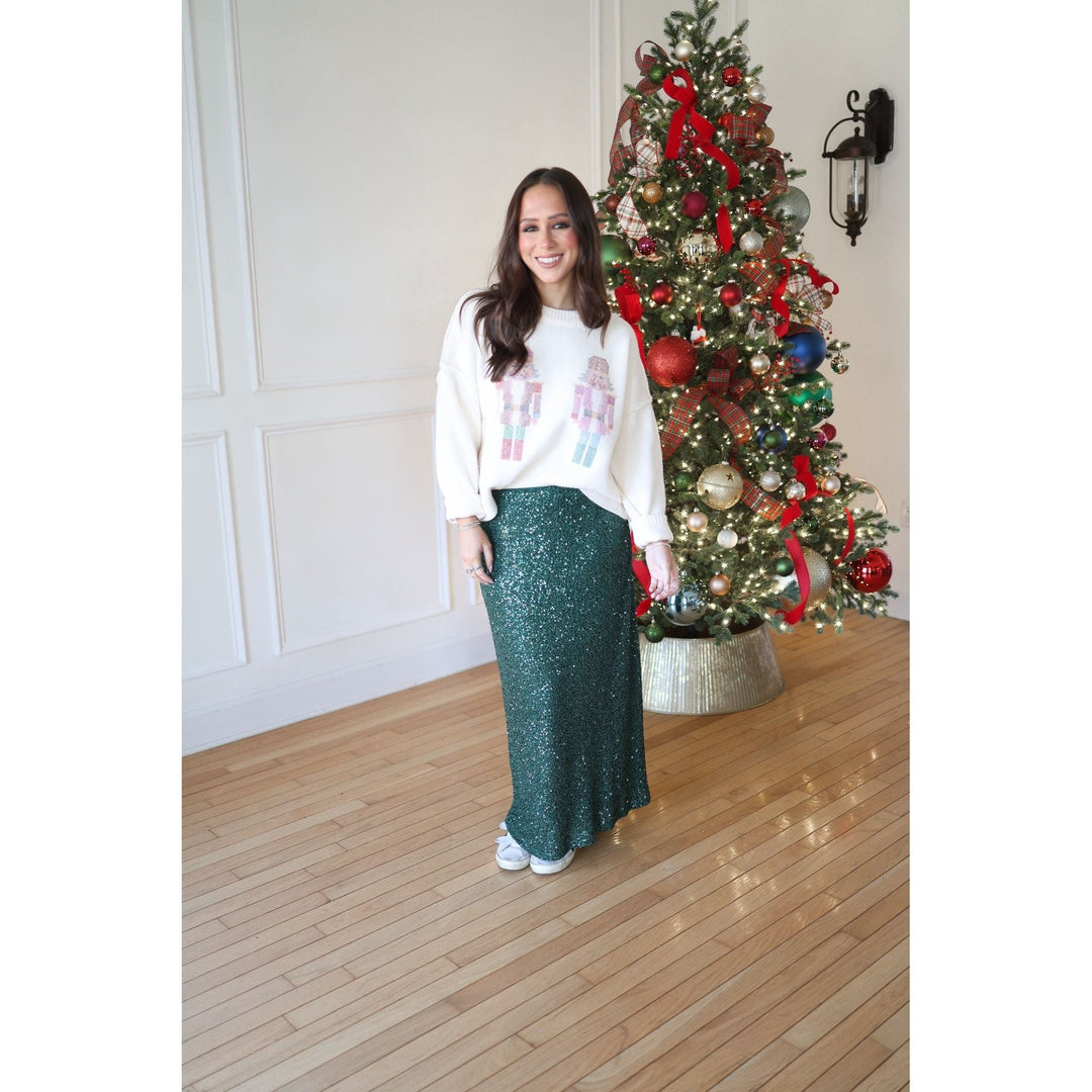 Woman in a white sweater and green skirt standing in front of a decorated Christmas tree.