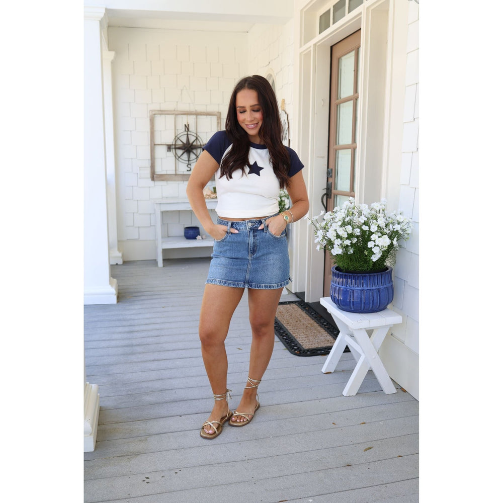 Woman in a casual outfit standing on a porch with a white door and wooden floor.