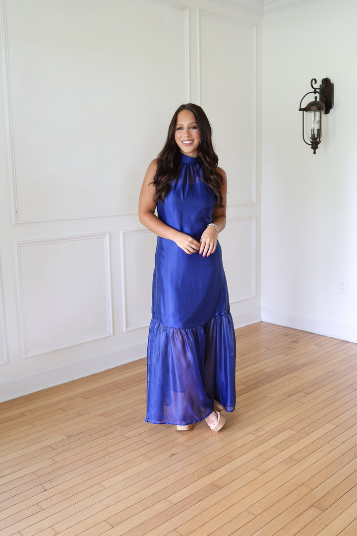 A woman wearing a sleeveless royal blue satin halter maxi dress with a ruffled hem
