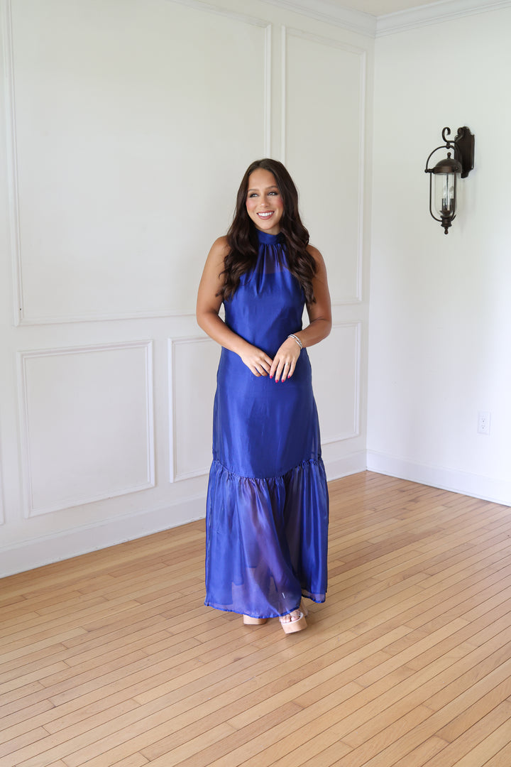 A woman wearing a sleeveless royal blue halter-neck maxi dress with a tiered skirt