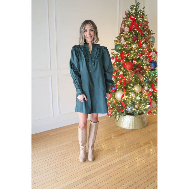 Woman in a teal dress standing next to a decorated Christmas tree indoors.