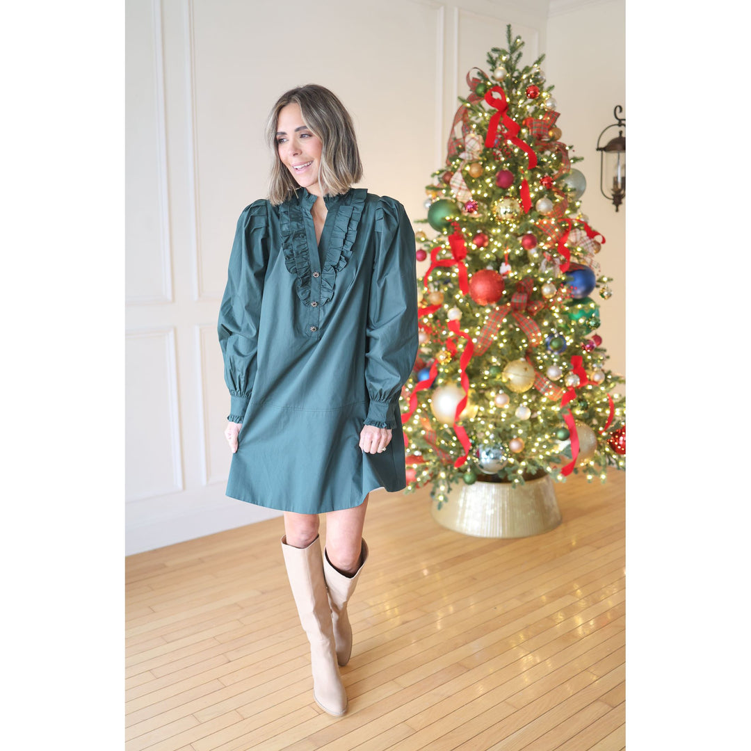 Woman in a teal dress standing in front of a decorated Christmas tree.