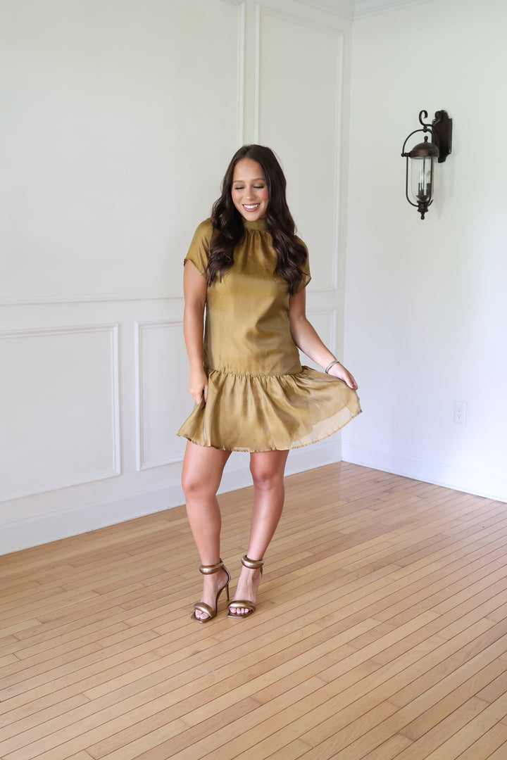 A woman modeling a short-sleeve, high-neck, ruffled mini dress in a metallic mustard gold color