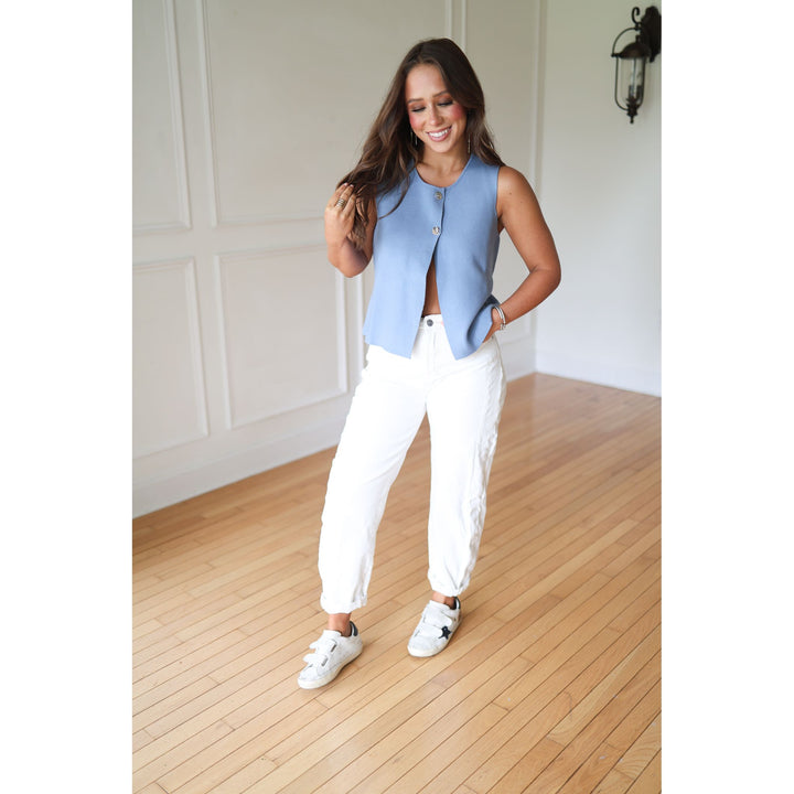 Woman wearing a light blue sleeveless jacket, white pants, and white sneakers 