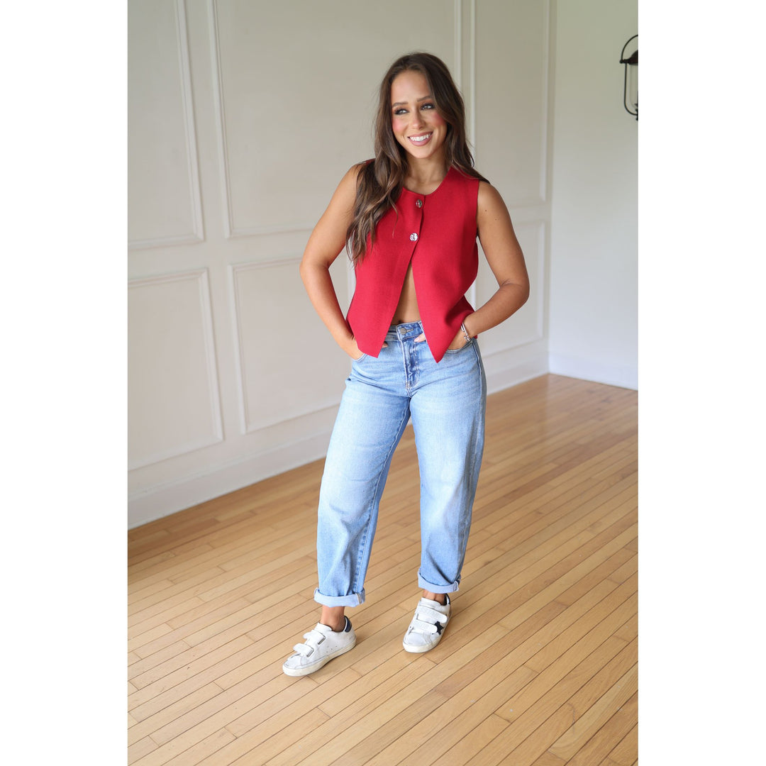 Woman wearing a red vest, blue jeans, and white sneakers 