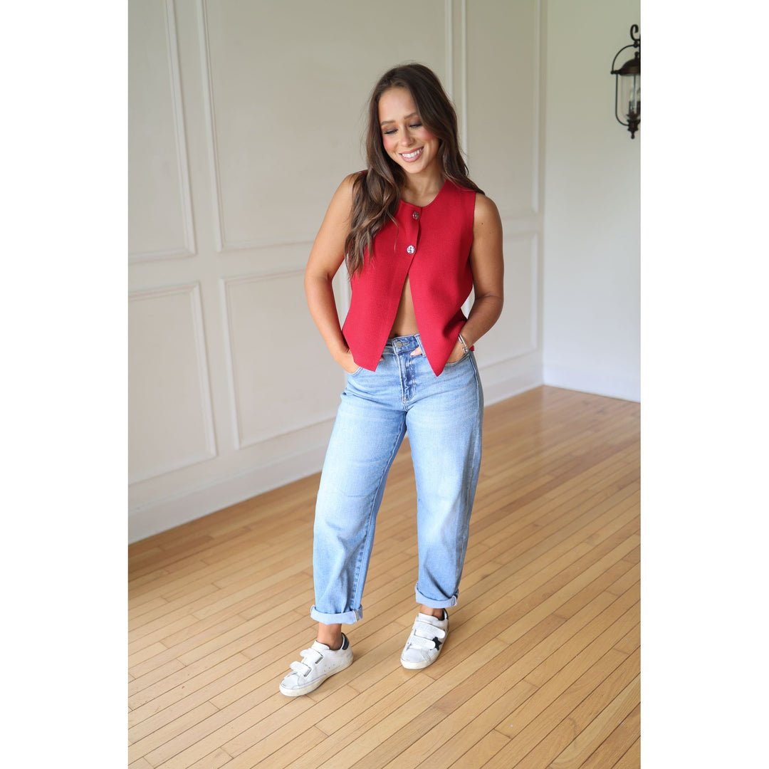Woman wearing a red sleeveless vest, blue jeans, and white sneakers 